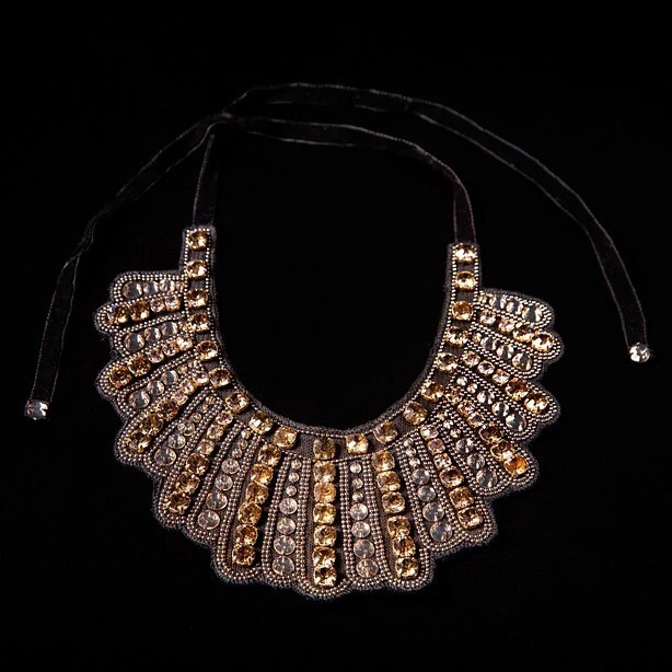 Close-up studio shot of an ornate statement necklace with amber and clear gems on a black velvet tie against a dark background.