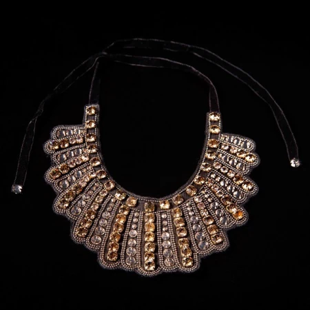 Close-up studio shot of an ornate statement necklace with amber and clear gems on a black velvet tie against a dark background.
