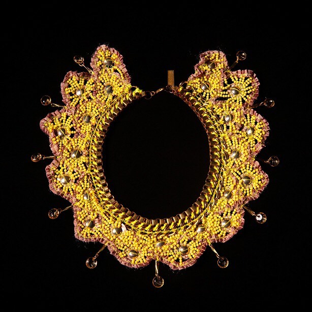 Artisan-crafted beaded collar necklace, featuring yellow beads, gold trim, and amber glass bead accents, against a stark black backdrop.