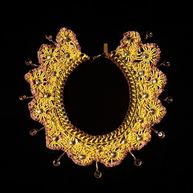 Artisan-crafted beaded collar necklace, featuring yellow beads, gold trim, and amber glass bead accents, against a stark black backdrop.