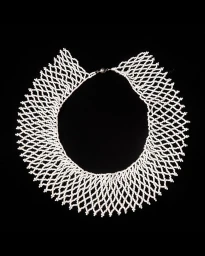 An intricate white beaded collar necklace displayed flat against a solid black background, photographed by Elinor Carucci.