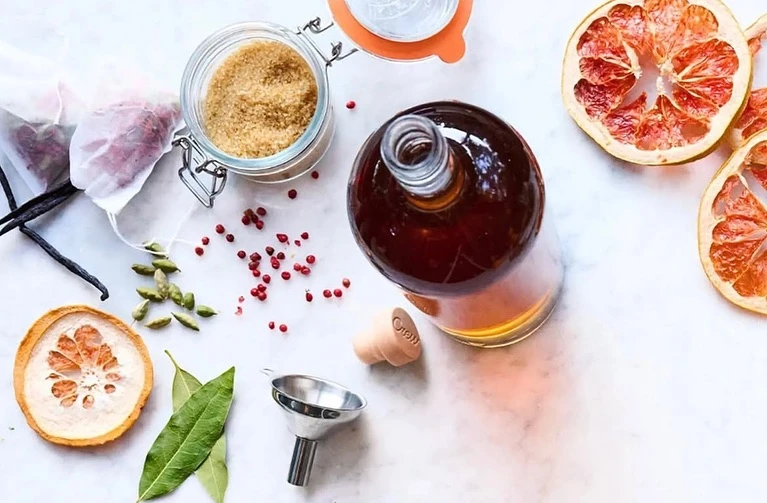 Overhead shot of a bottle, sugar, spices, and grapefruit slices arranged on a marble surface, creating a visually appealing food still life.