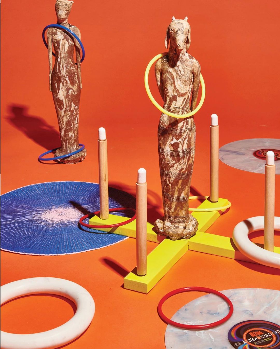 Ring toss game setup with wooden figures and colorful rings on an orange backdrop, creating a playful and artistic composition.