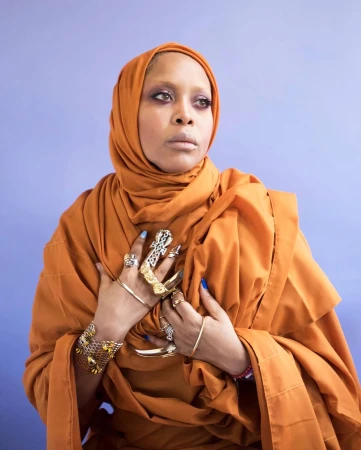 Portrait of a Black woman wearing an orange hijab and layered metallic rings against a purple background