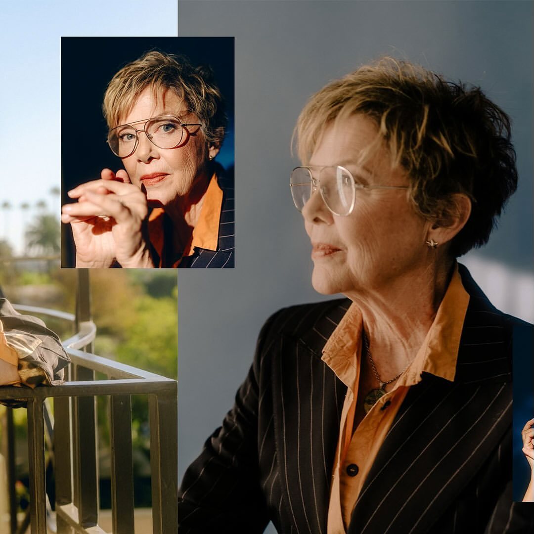 Mature woman in pinstripe suit and glasses poses in front of a city view, captured in a soft studio shot.