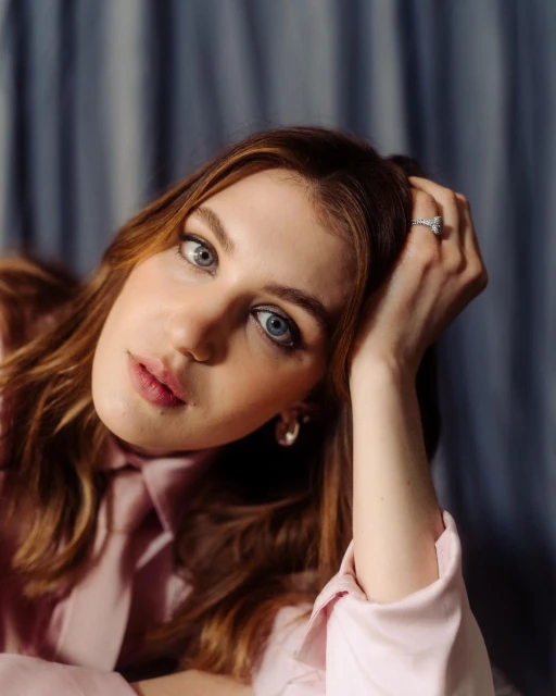 Portrait of a woman with auburn hair in a pink shirt, soft lighting, and a blue draped background, beauty, fashion.