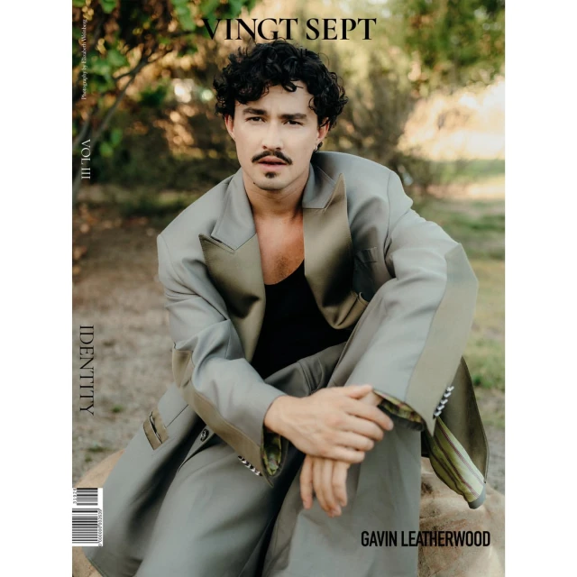 Magazine cover featuring a man in an oversized suit, seated outdoors with a neutral backdrop of trees and natural light.