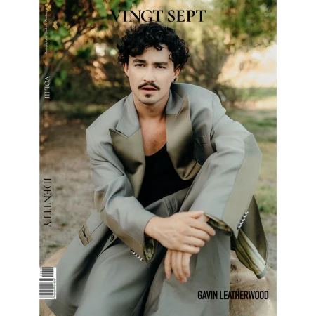 Magazine cover featuring a man in an oversized suit, seated outdoors with a neutral backdrop of trees and natural light.