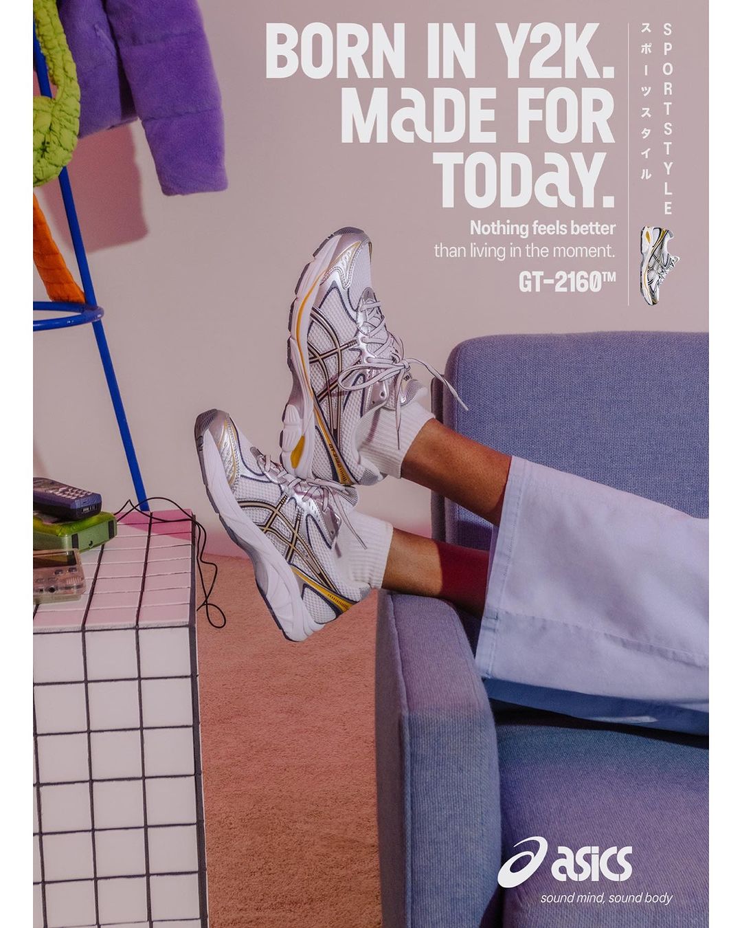White and silver Asics sneakers are displayed against a pale pink background, styled with a denim blue armchair and other colorful props.