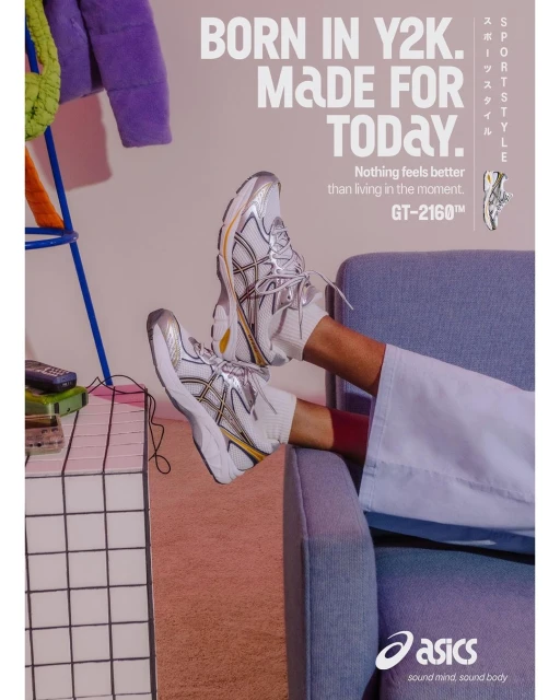 White and silver Asics sneakers are displayed against a pale pink background, styled with a denim blue armchair and other colorful props.