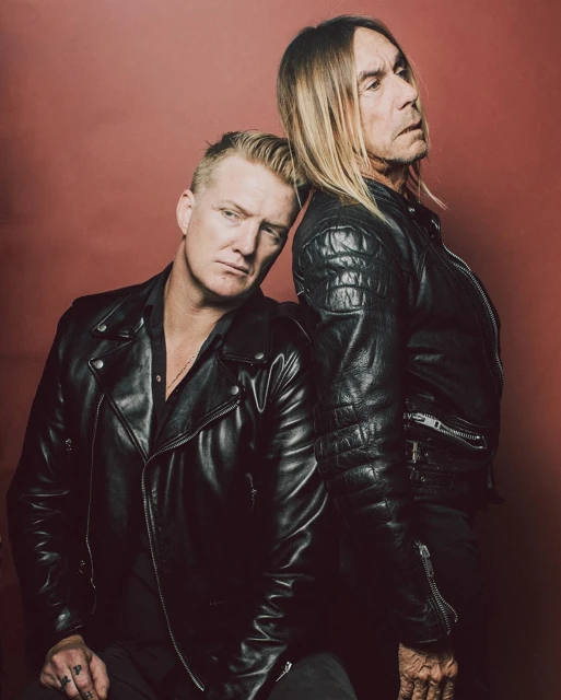 Close-up studio portrait of two adult men, one with his head resting on the other's shoulder, both wearing black leather jackets.