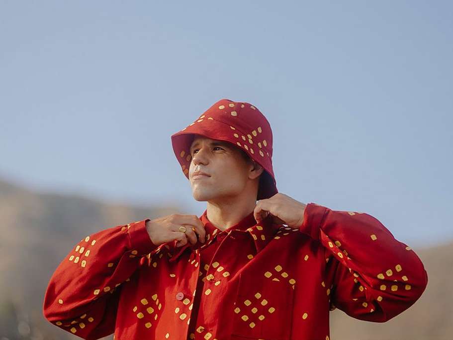 Portrait of a man wearing a red patterned button-down shirt and bucket hat, gazing upwards outdoors with a clear blue sky background.