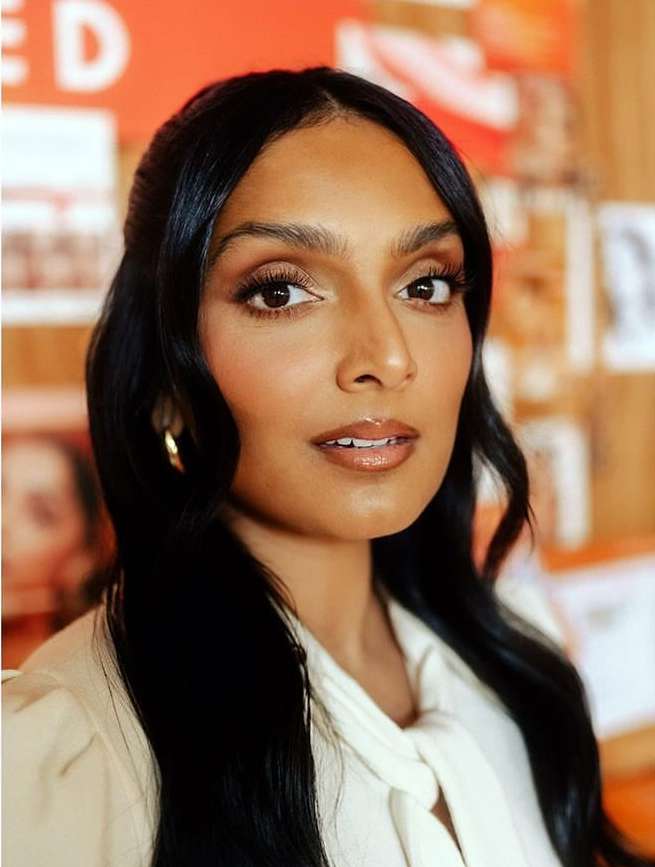 Close-up studio portrait of an adult woman with long black hair, light skin, wearing a white collared shirt and gold hoop earrings.