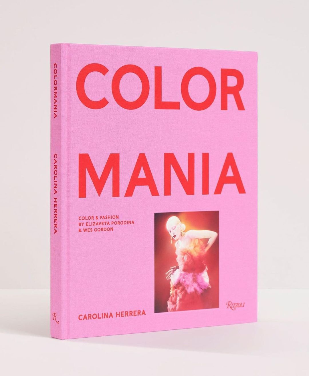 Fashion book titled 'Color Mania' by Carolina Herrera featuring a model in colorful fashion, set against a light pink background and studio lighting.