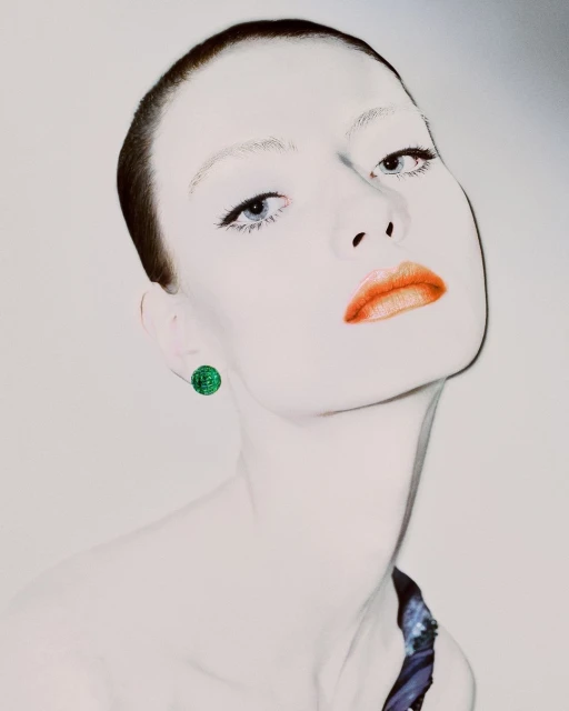 Close-up portrait of a fair-skinned adult female with short brunette hair, blue eyes, and coral lipstick, wearing a green round earring.