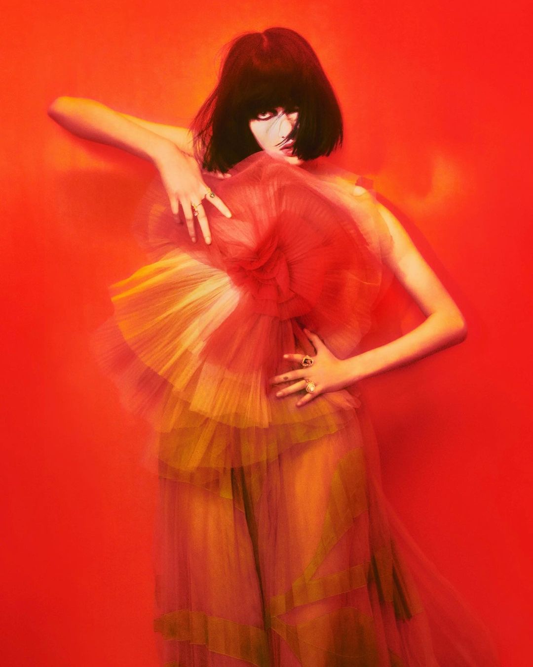Artistic portrait of a woman with dark hair wearing a layered dress in a red studio. Fashion editorial with dramatic lighting.