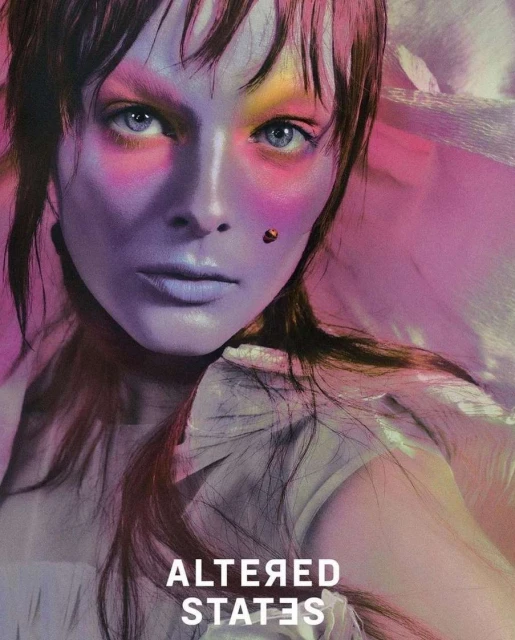 A close-up shot features a model with unique makeup in vibrant purples, pinks, and yellows, complemented by fair skin and light eyes.