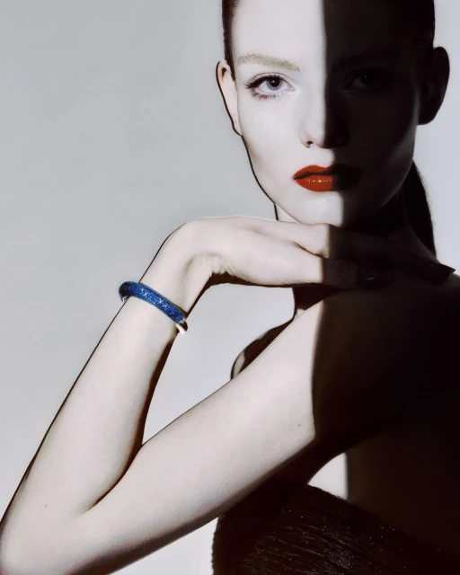 Close-up fashion shot of a fair-skinned woman wearing red lipstick and a sparkly blue bracelet in a studio setting with strong shadows.
