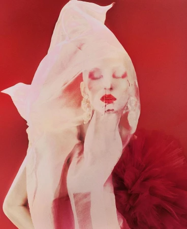 Artistic fashion portrait of a person with face paint and sheer fabric on a red background, showcasing creative beauty styling.