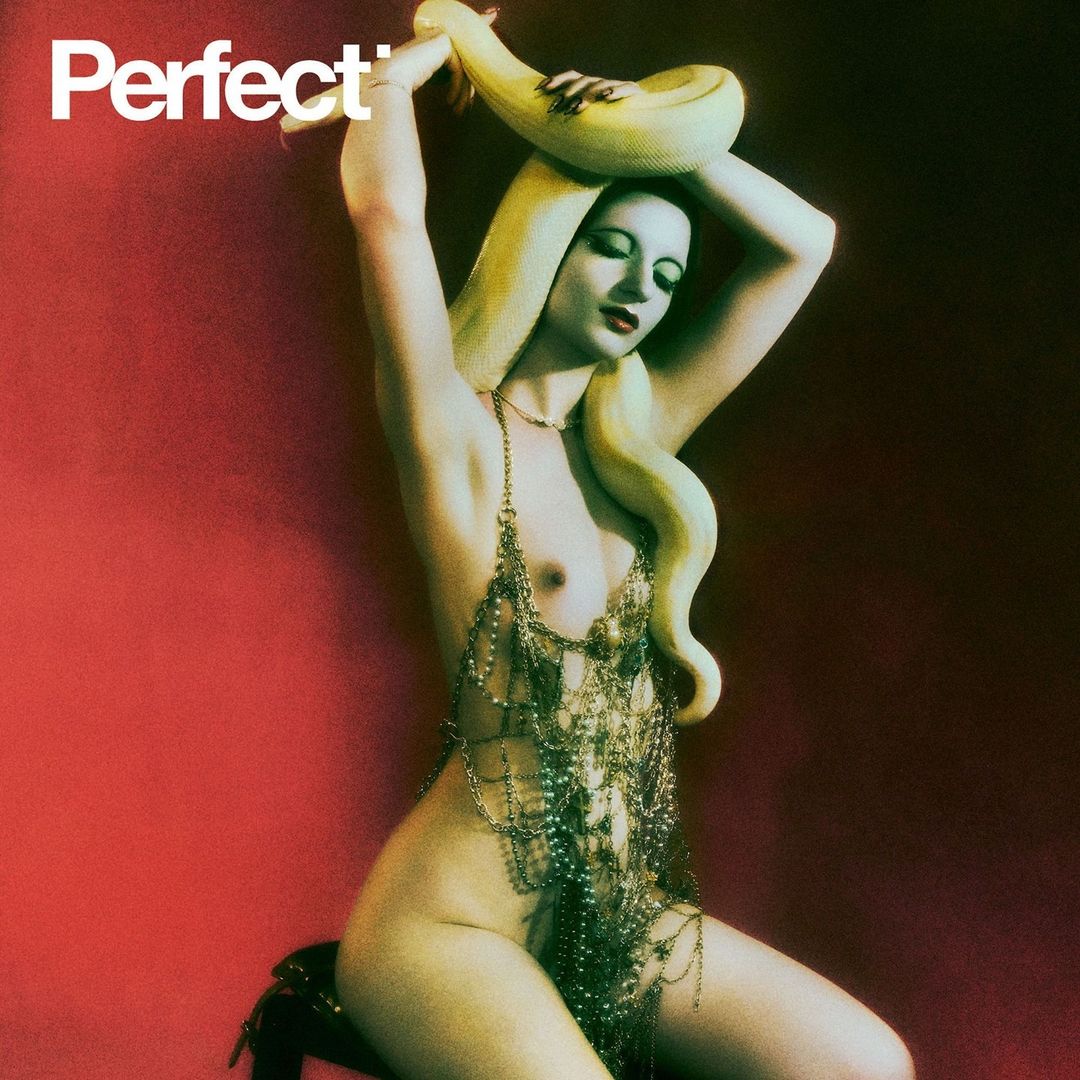 A nude woman adorned with jewelry and a snake poses seductively against a red backdrop, showcasing fashion and beauty.