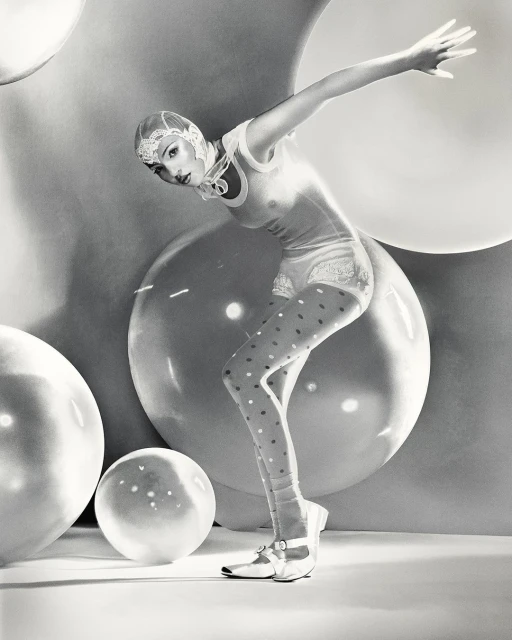 Woman in vintage-style bathing suit and polka-dot stockings poses among large, translucent spheres in a black and white studio portrait.