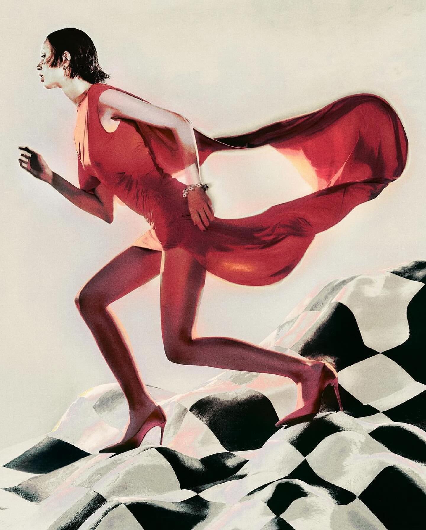 Elegant woman in motion wearing a red dress and heels, a flowing cape, set against a black and white checkered surface.