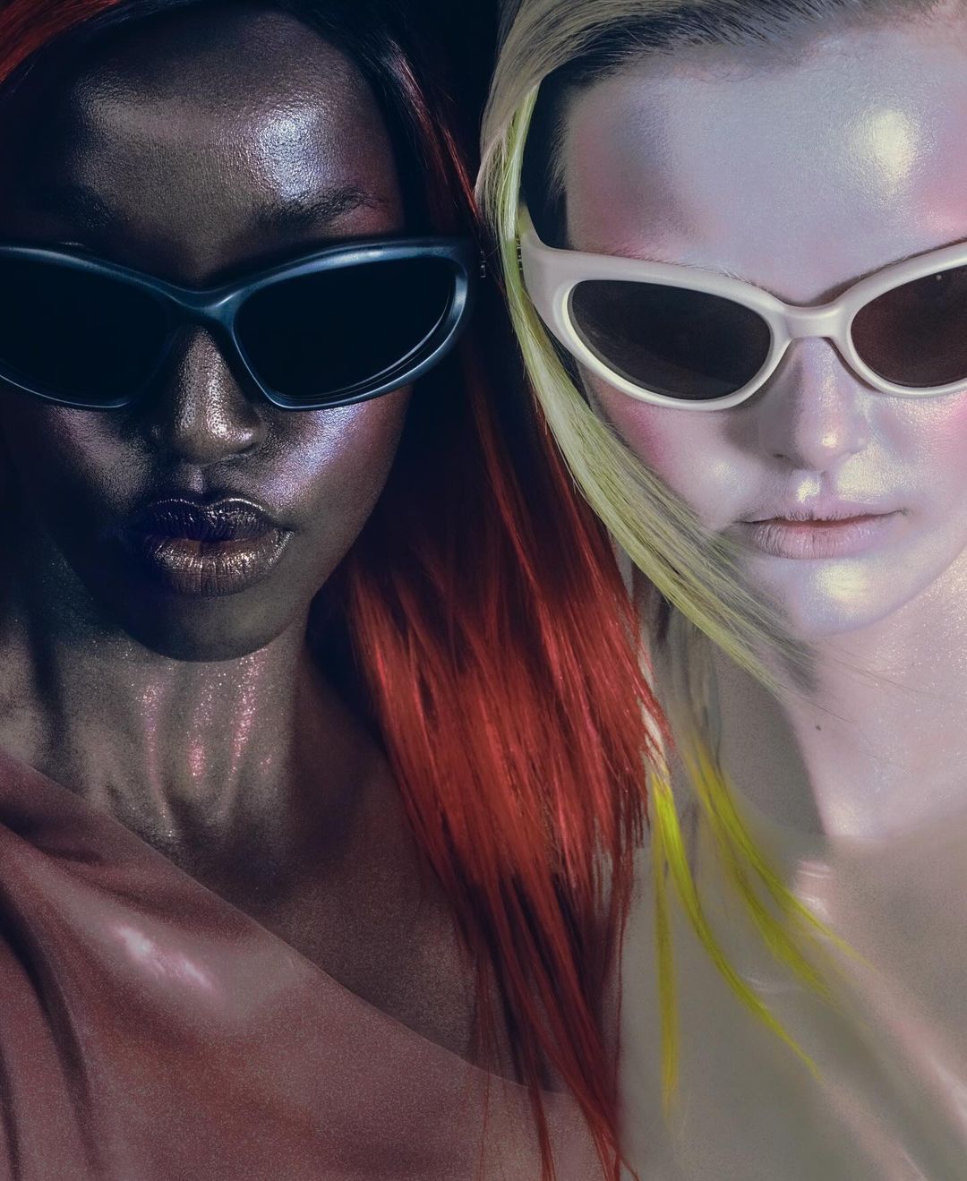 Two fashion models with red and yellow hair wearing futuristic sunglasses in a studio. Beauty and fashion editorial shot.