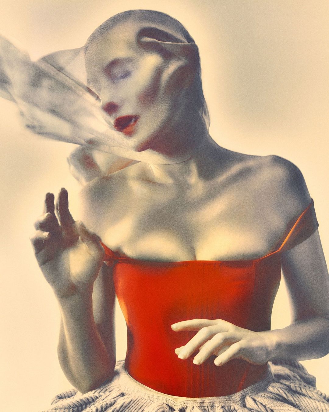 Fashion shot of a fair-skinned adult female wearing a red corset and white ruffled skirt, face partially covered by sheer white fabric.