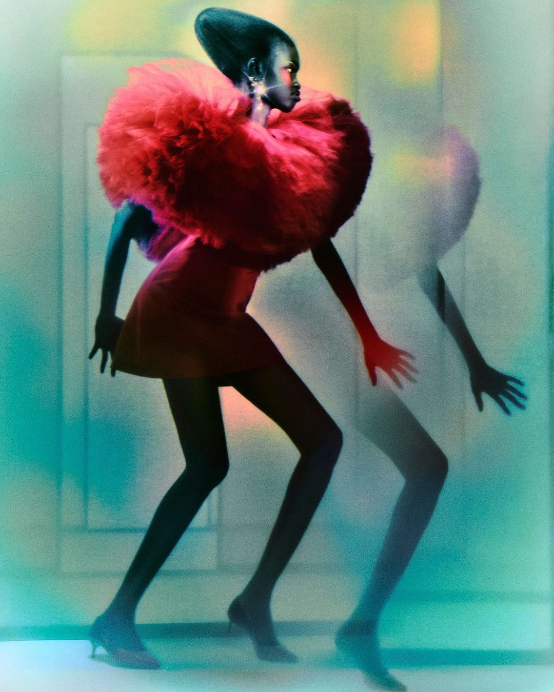 Fashion shot of African American model with red dress and large ruffled collar posing with blurred ghost image in gradient lighting.