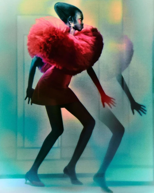 Fashion shot of African American model with red dress and large ruffled collar posing with blurred ghost image in gradient lighting.