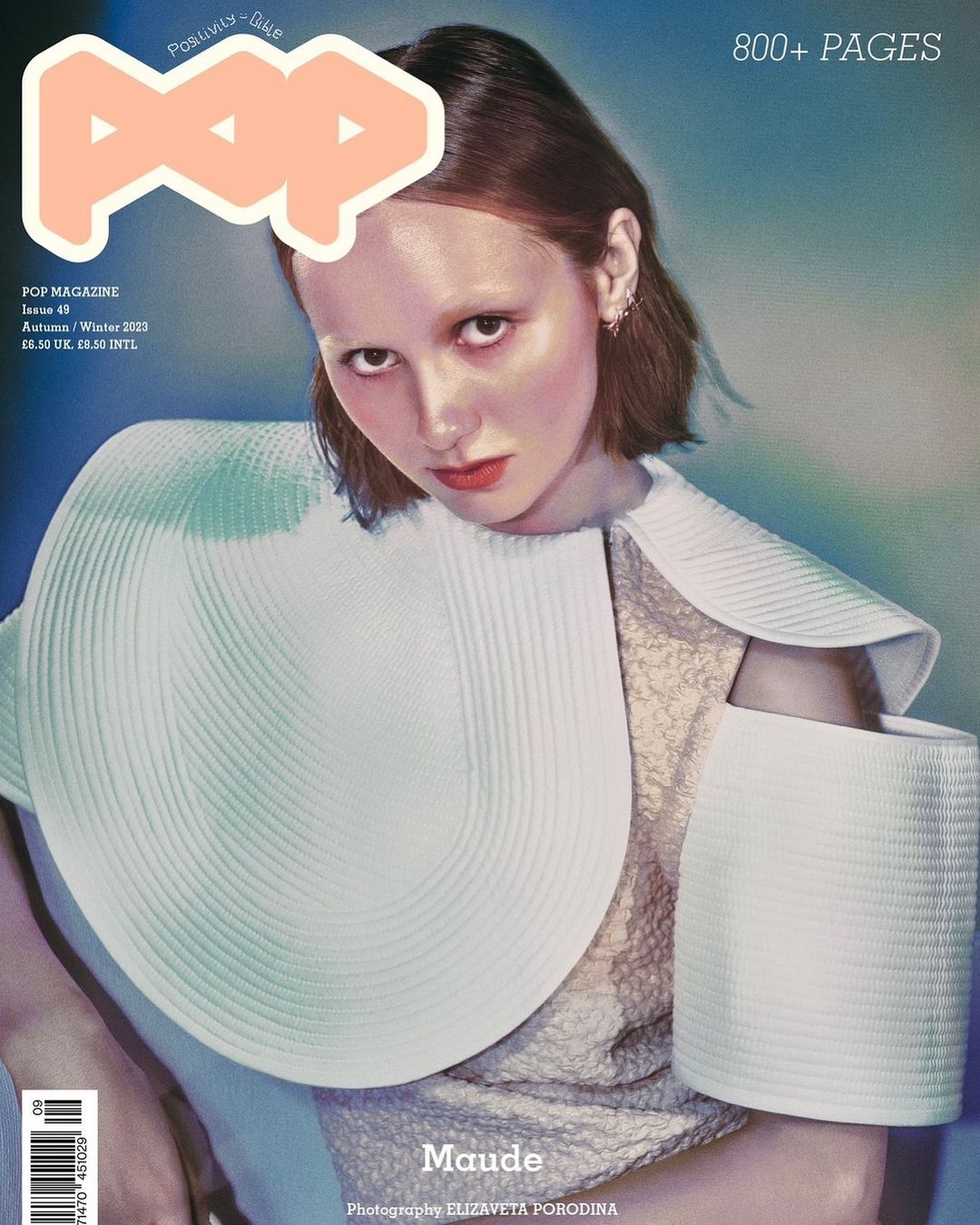Magazine cover featuring a fair-skinned young woman with red lipstick wearing a white textured outfit and a large white collar.