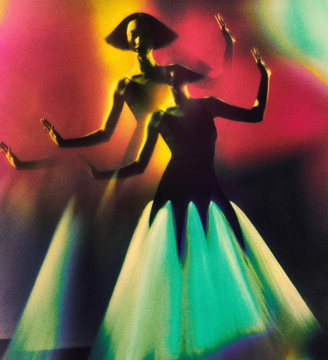 Fashion photo featuring an elegant adult woman in a dress with a flared skirt, posing with arms raised against a vivid, blurred background.