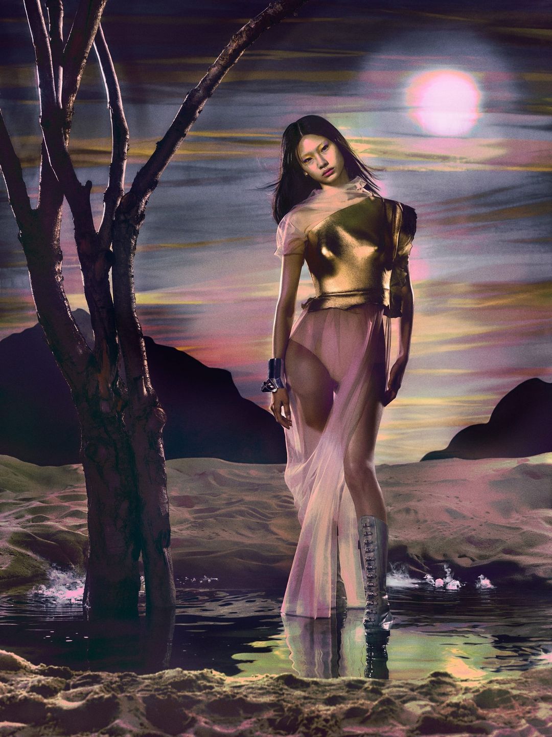 A young woman in a gold top and silver boots poses near a dead tree in a surreal, moonlit landscape for a fashion editorial.