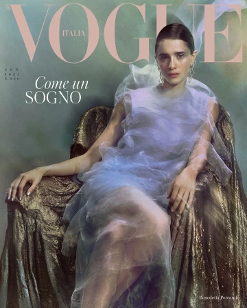 A woman in a sheer light blue dress seated in a textured gold armchair against a moody green background