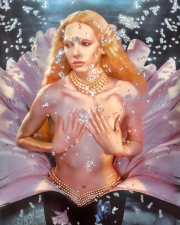 Androgynous model adorned with shimmering glitter and jewelry poses in a floral setting, wearing pearl body jewelry, against a dark background.