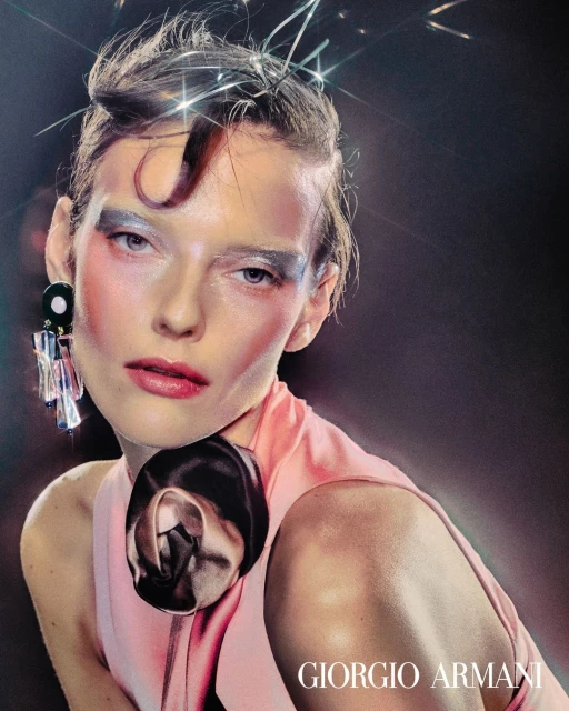 Close-up fashion portrait of a woman with stylized make-up and earrings wearing a pink dress against a dark background.