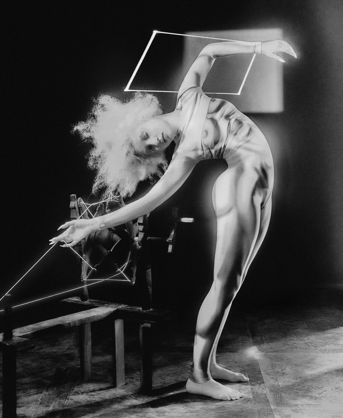 Black and white photograph of an adult female in a pose with a wooden structure and string, artful and mysterious lighting.