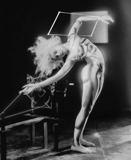 Black and white photograph of an adult female in a pose with a wooden structure and string, artful and mysterious lighting.