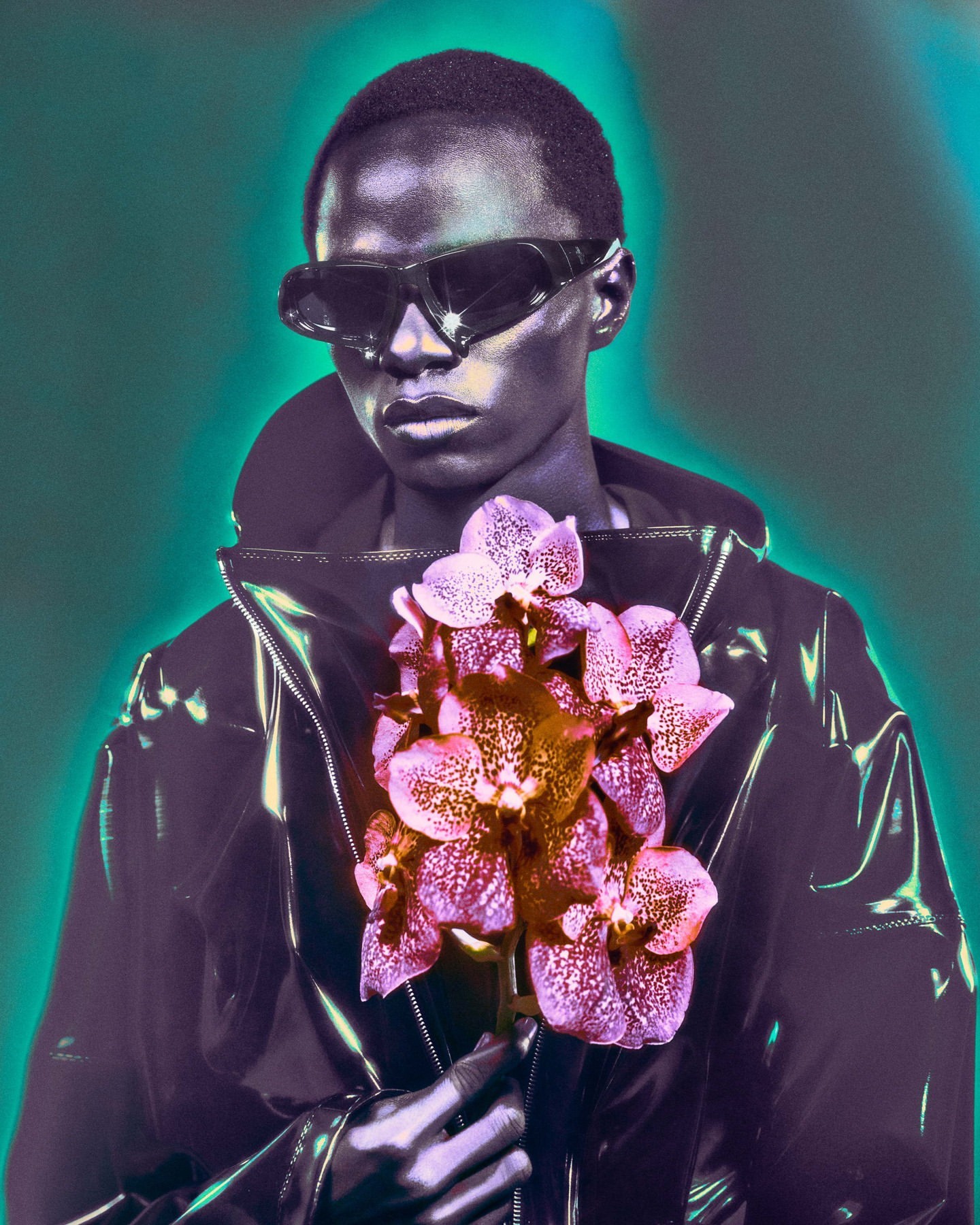 Portrait of Black male model in sunglasses and black coat holding pink orchid flowers against teal background in studio lighting.