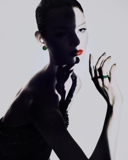 Close-up studio shot of a fashionable adult woman in an elegant black dress and green jewelry, with dramatic lighting and makeup.