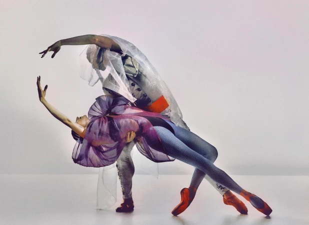 Two ballet dancers in a studio. One dancer holds the other in a pose with artistic costumes and pointe shoes, on a white background.