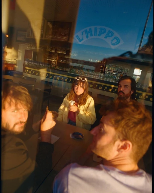 Four people are seated around a table at a restaurant behind a glass window during the evening, with a glimpse of the outside environment.