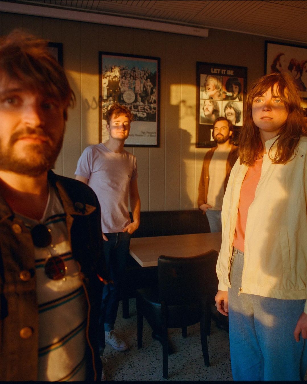 Four people stand inside a diner with Beatles posters, bathed in the warm light of golden hour, creating a vintage, retro feel.