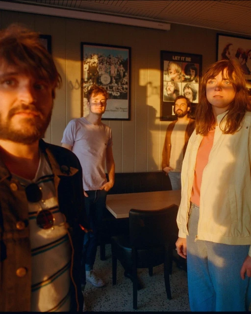 Four people stand inside a diner with Beatles posters, bathed in the warm light of golden hour, creating a vintage, retro feel.