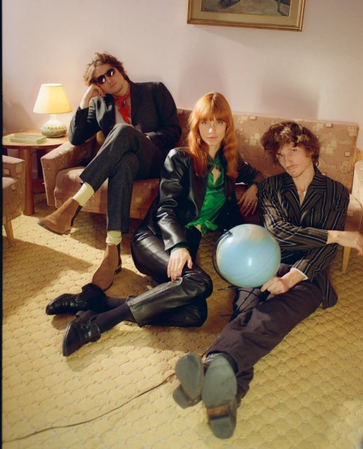 Three young adults in stylish vintage clothing are posing indoors with a globe, illuminated by a lamp in a retro interior.