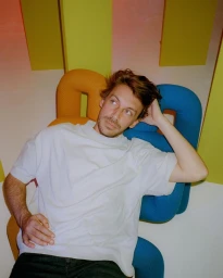 Man in a white t-shirt sitting against colorful abstract sculptural furniture in Paris photographed by Ella Hermë