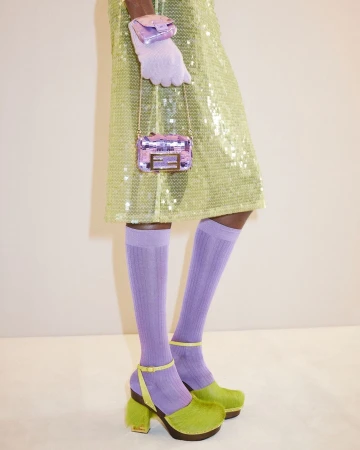 A fashion shot showcasing a sequined chartreuse dress, lavender socks, handbag, glove, and green platform shoes against a neutral background.