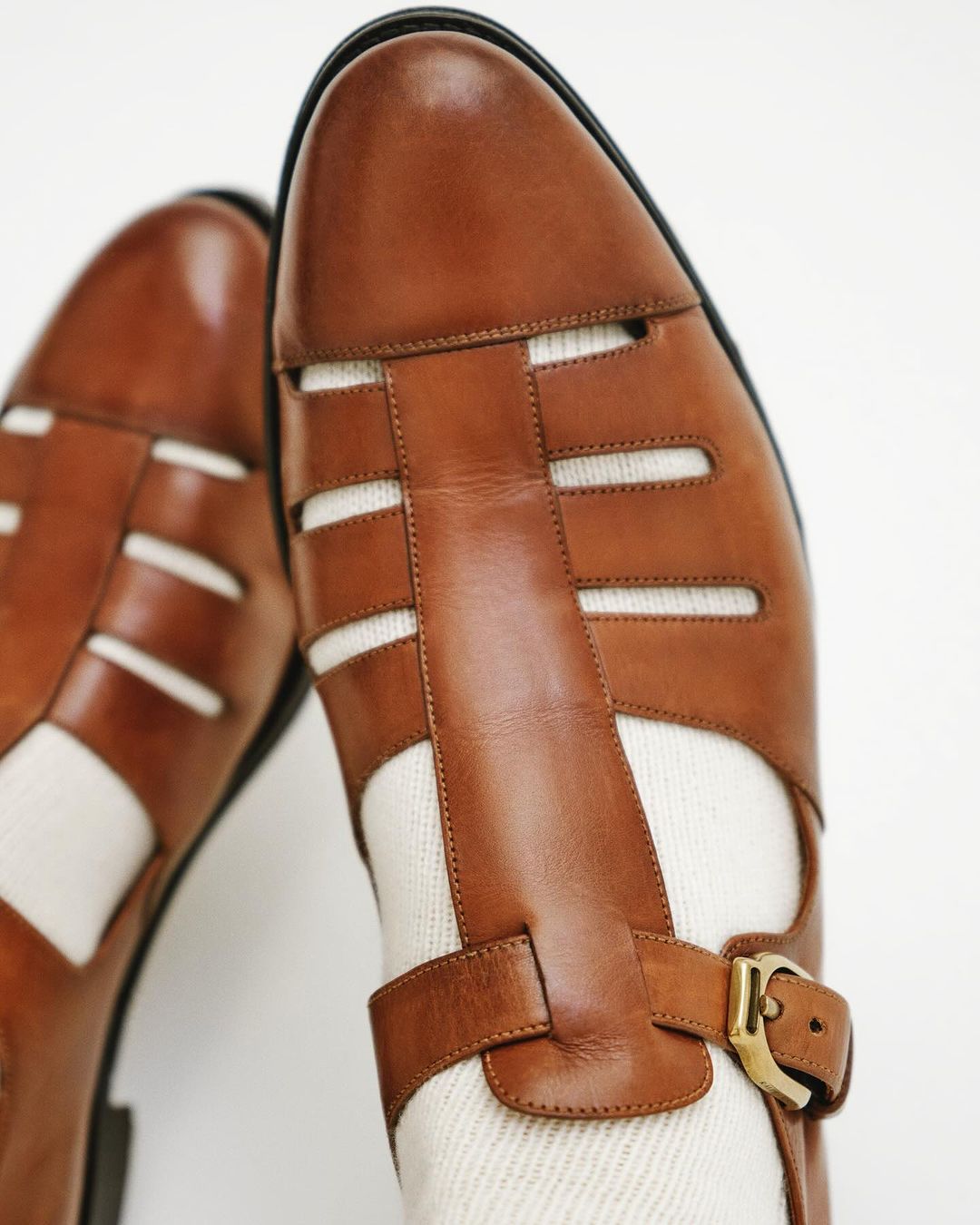 Close-up of brown leather fisherman sandals with buckle, paired with cream-colored socks, against a plain white backdrop.