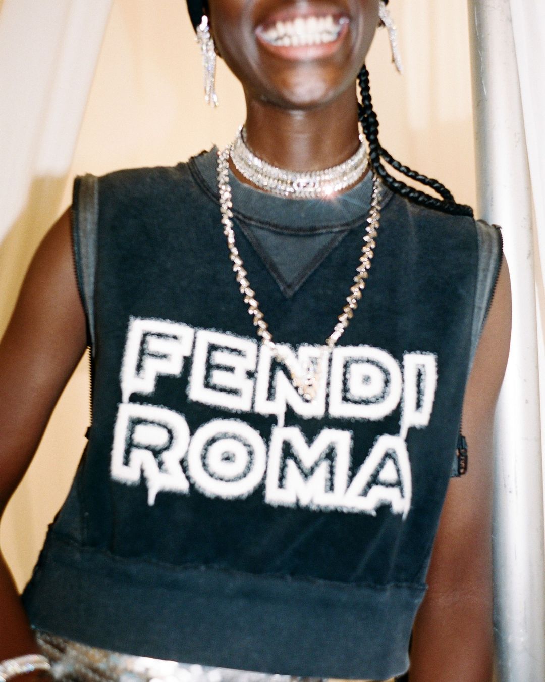 Close-up shot of a Black female model wearing a Fendi Roma crop top, jewelry and a headscarf. She is smiling in a studio.