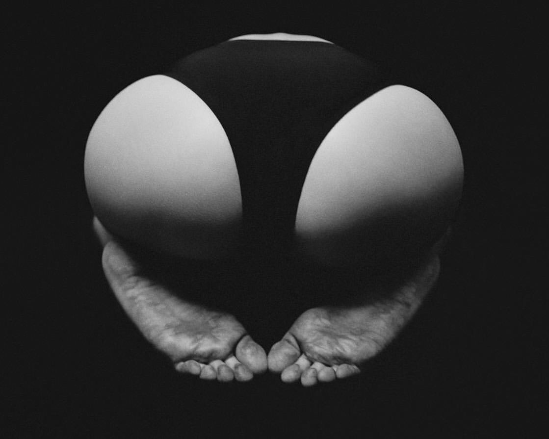 Close-up black and white photo of a person in dark bottoms with bare feet, against a dark background, creating a striking contrast.